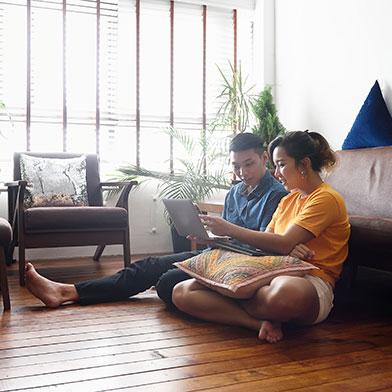a couple sitting on their living room floor pointing something out on a laptop